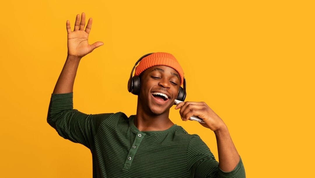A man with headphones dances and sings against a bright yellow background.